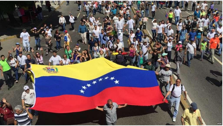 Anti-Maduro protesters in the streets with a huge Venezuelan flag.