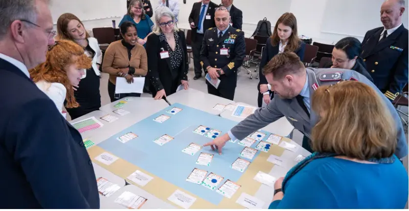 A bunch of people, some in uniform, meeting around a table with a war game on it.